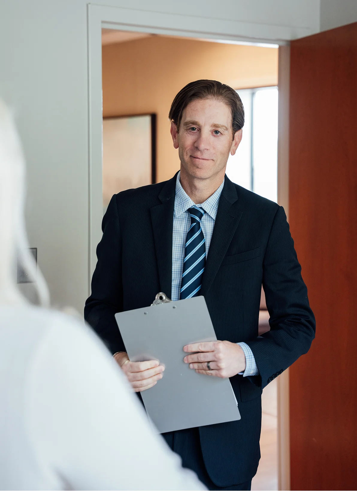 Dr Rottman MD in navy suit holding documents standing in modern office doorway - in Owings Mills, MD