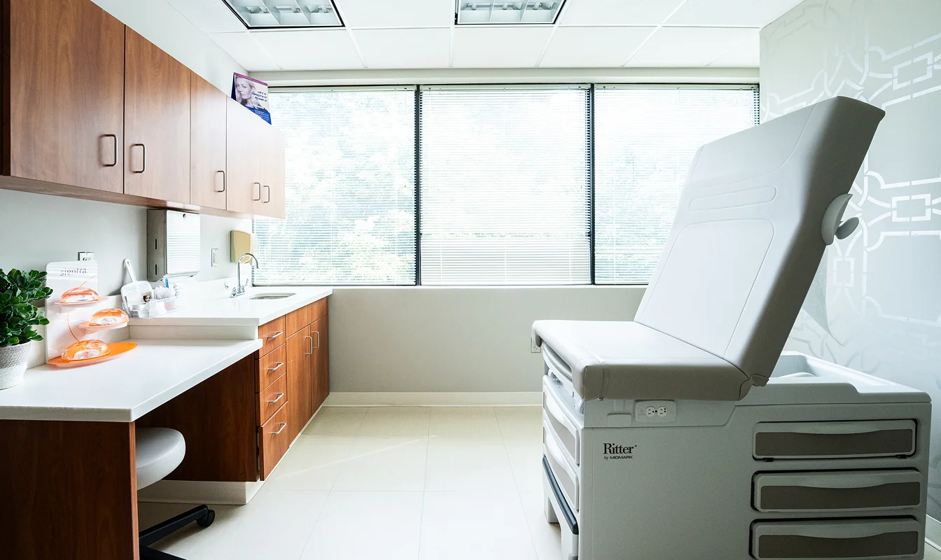 Modern medical examination room with exam table, cabinets, counter, and natural light from large windows