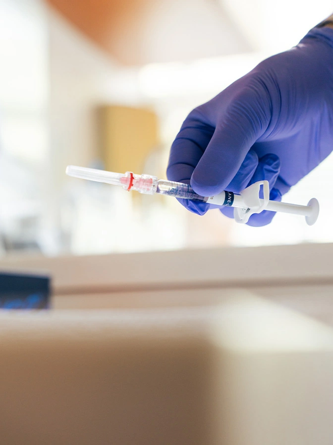Medical professional in blue glove holding syringe with pink medication for injection or vaccination - Botox in Owings Mills, MD