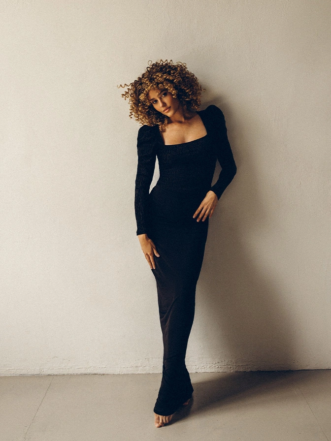 Woman in elegant black long-sleeve jumpsuit with curly hair posing against neutral wall - Bear implant illness in Owings Mills, MD