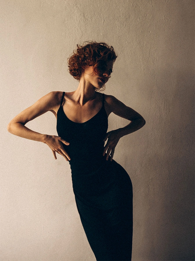 Elegant woman in black dress with dramatic lighting and shadow effect against neutral wall - Body lift in Owings Mills, MD