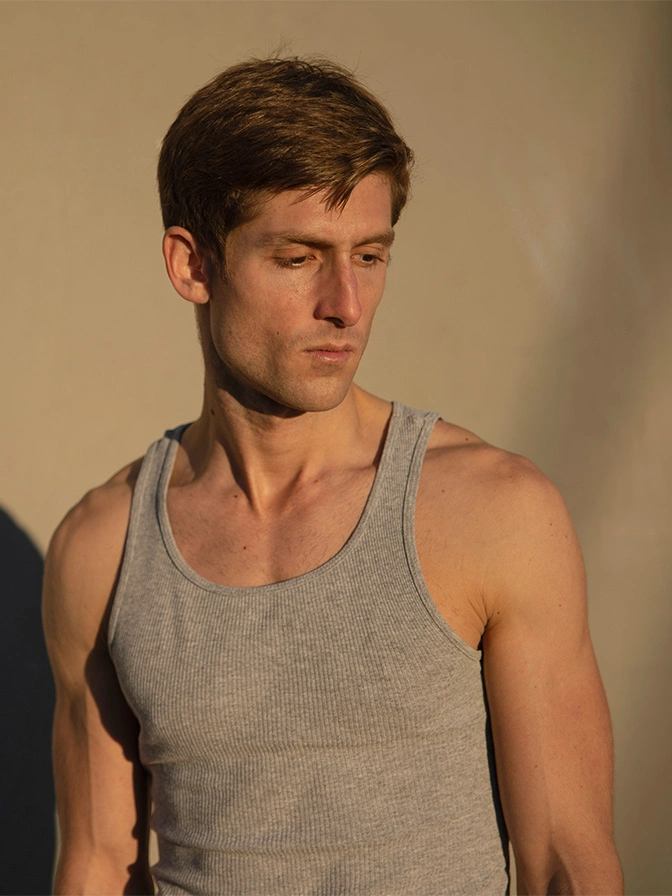 Young man in gray tank top looking down pensively against neutral background - Male chest lift in Owings Mills, MD