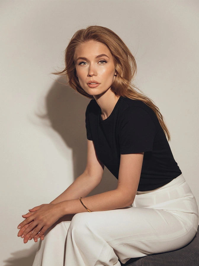 Young woman in black top and white pants sitting against neutral background in natural lighting - Skinceuticals in Owings Mills, MD