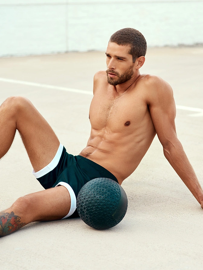 Fit man sitting on beach with foam roller doing recovery exercises in black shorts - Tummy tuck in Owings Mills, MD