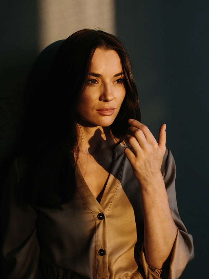 Woman with long dark hair in yellow cardigan posing with hand near face in warm sunlight - V1 peel in Owings Mills, MD