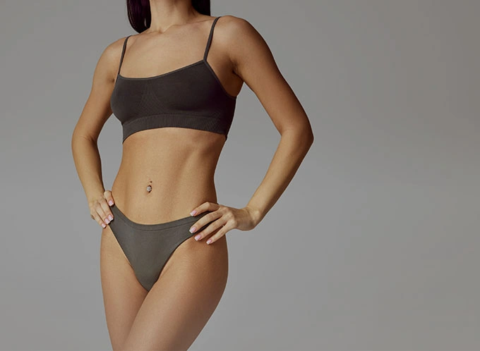 Woman wearing brown two-piece swimsuit standing against gray background showing fit body and summer beachwear style - Body lift in Owings Mills, MD