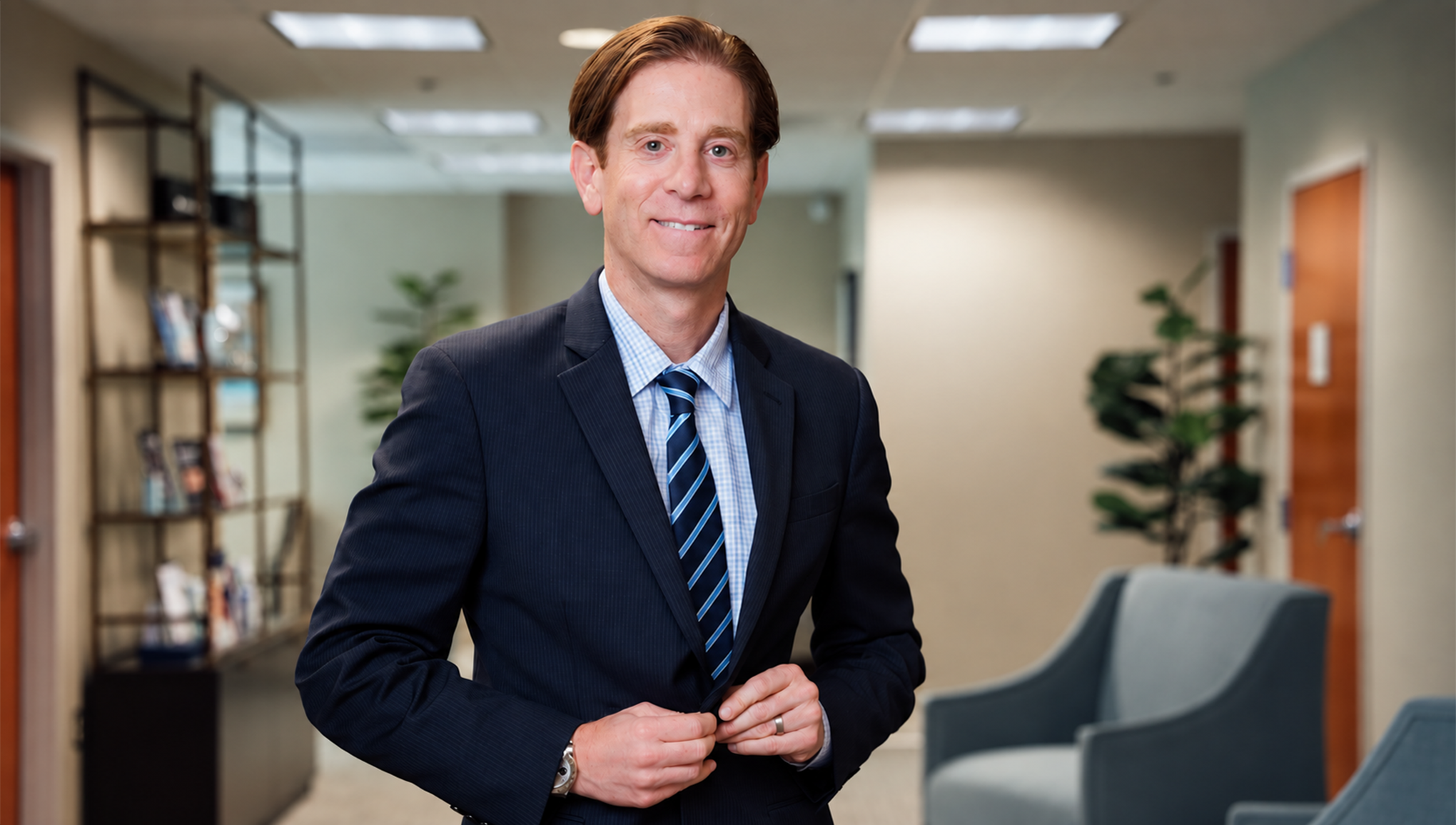 Dr Rottman MD in navy suit adjusting jacket in modern office setting with bookshelves and plants - in Owings Mills, MD