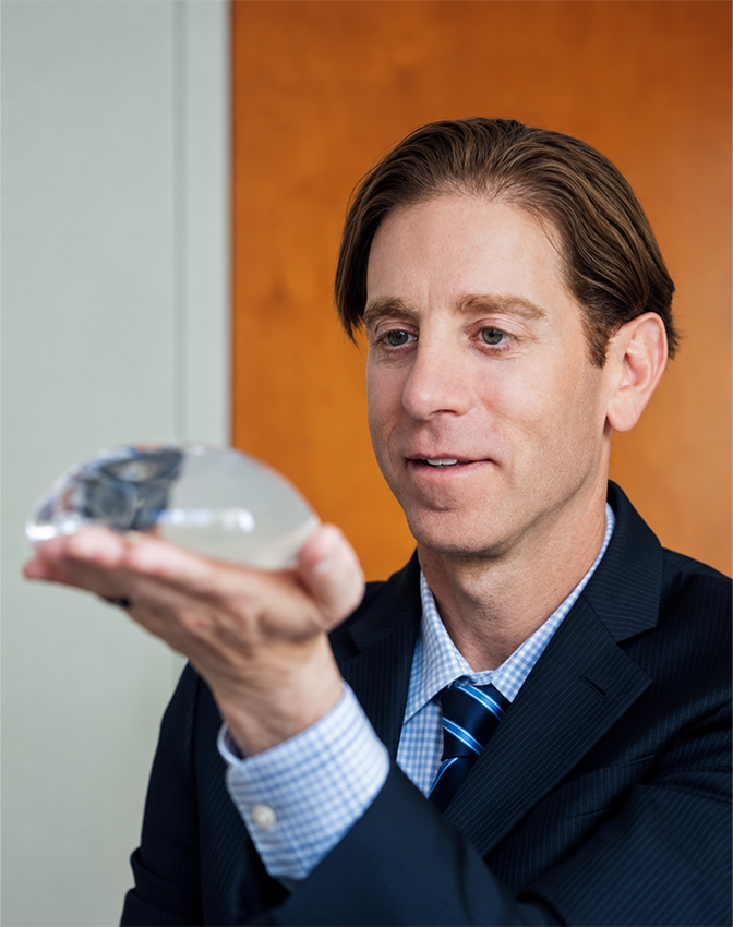 Dr Rottman MD in business attire holding breast implant while smiling at camera - Breast in Owings Mills, MD